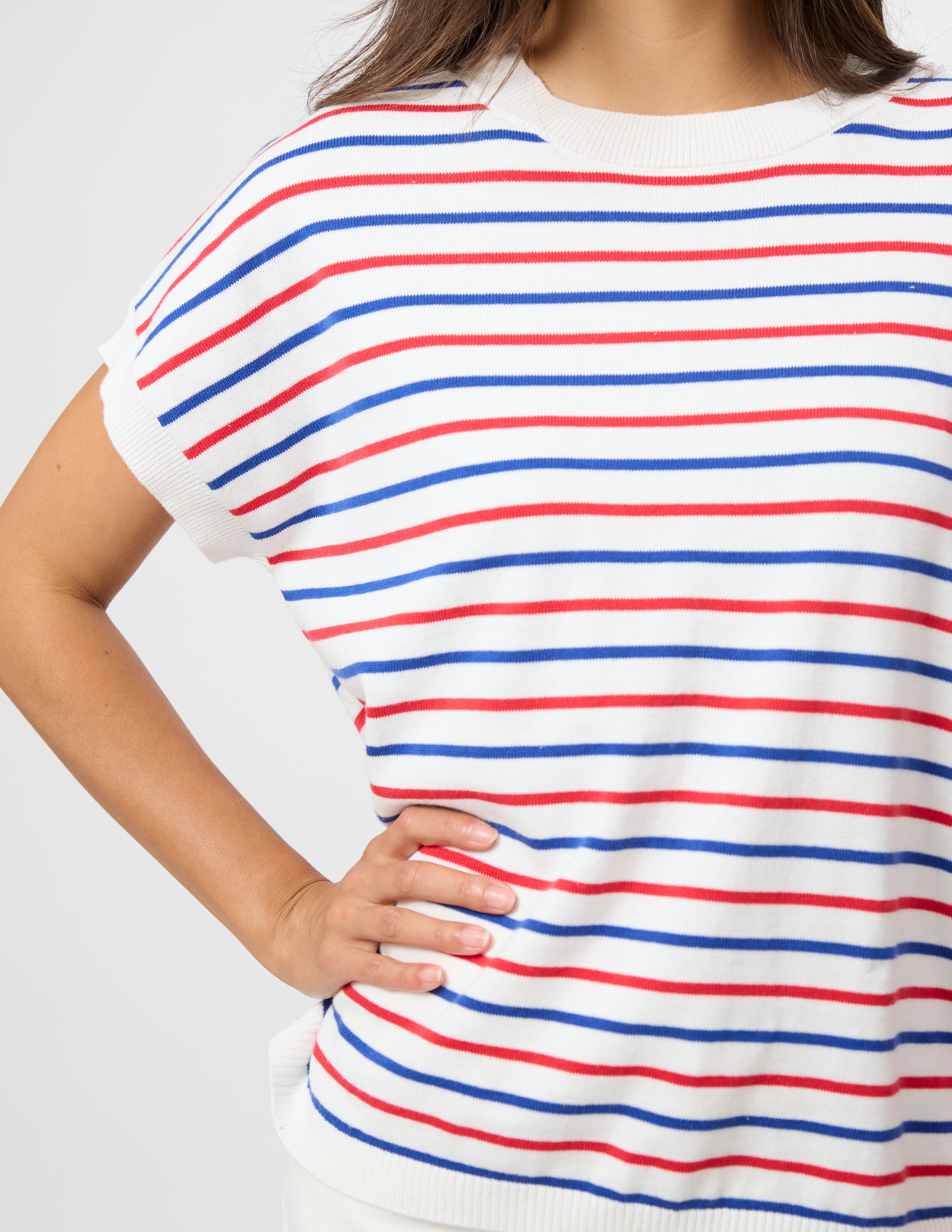 A close-up of a person wearing a short-sleeve knit top with horizontal red, blue, and white stripes against a light gray background.