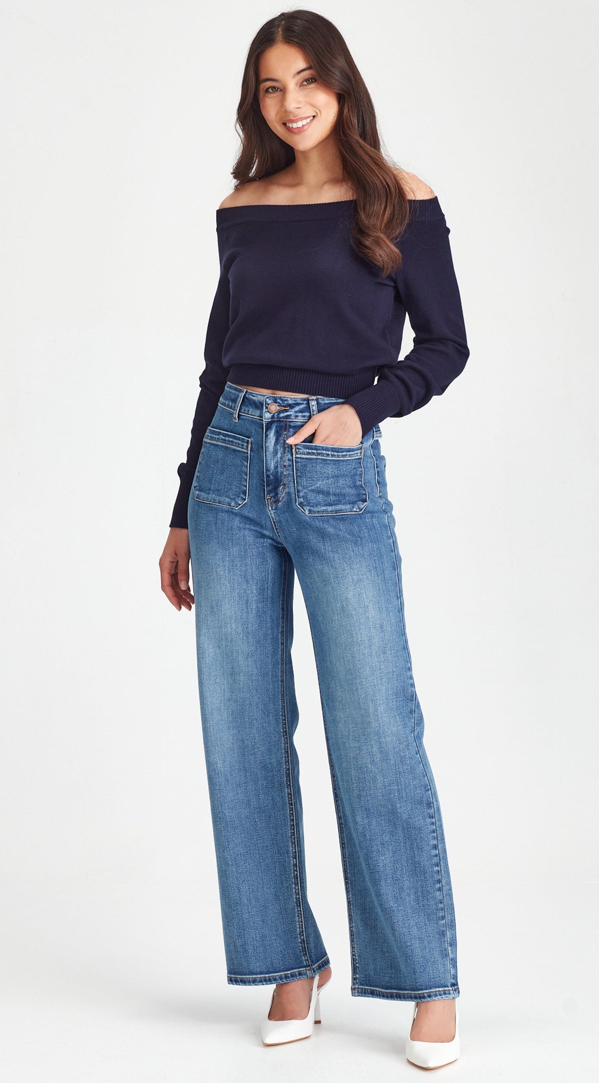 Woman wearing a navy off-shoulder top and blue jeans on a white background
