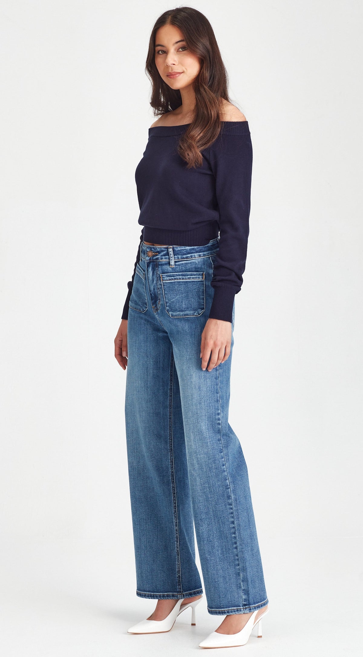 Woman wearing a navy off-shoulder top and blue jeans on a white background