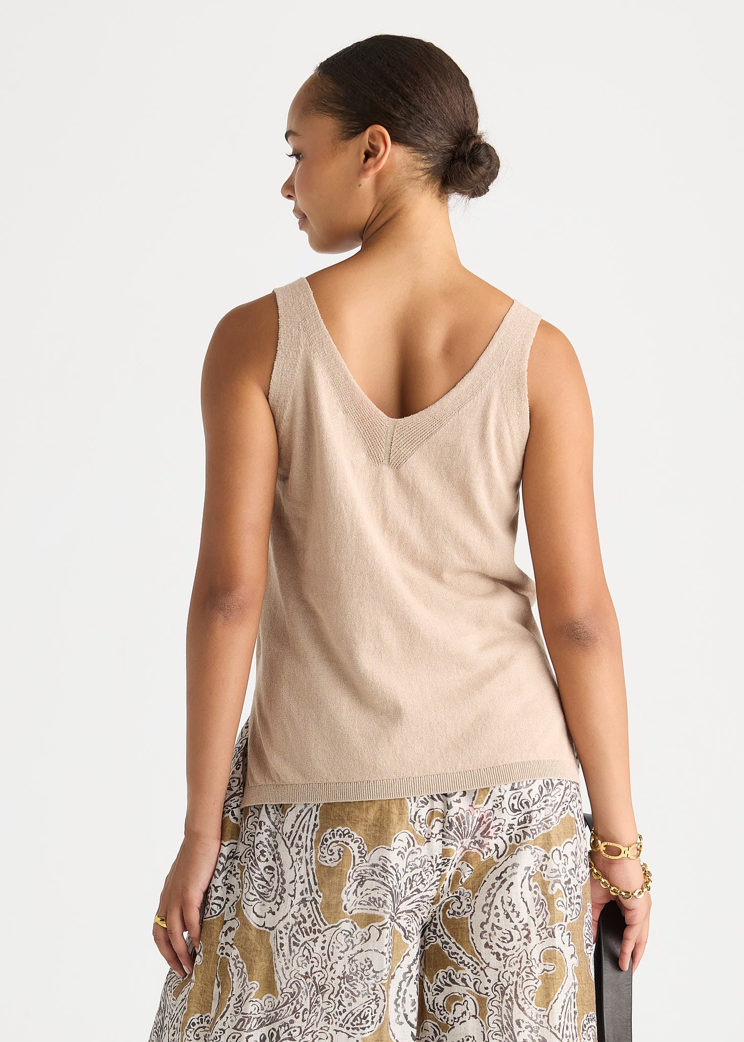 A woman shown from the back wearing a light beige knit tank top and patterned pants with a gold, white, and gray paisley design.
