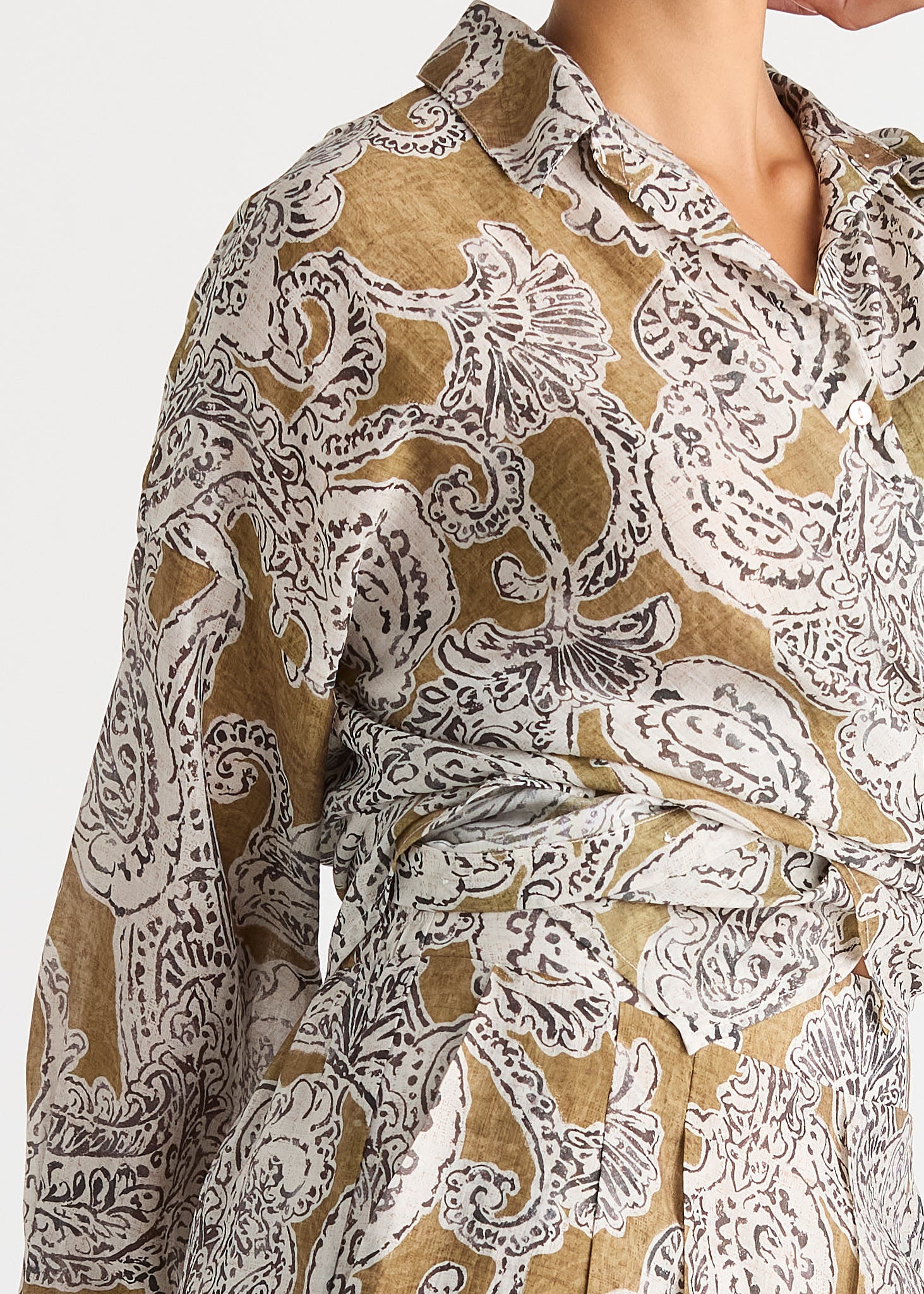 A close-up of a long-sleeve collared shirt dress with a brown and white paisley pattern, shown on a model against a light gray background.