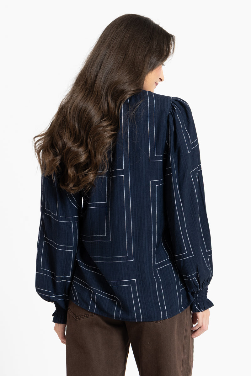Woman wearing a dark blue blouse with white geometric patterns on a white background