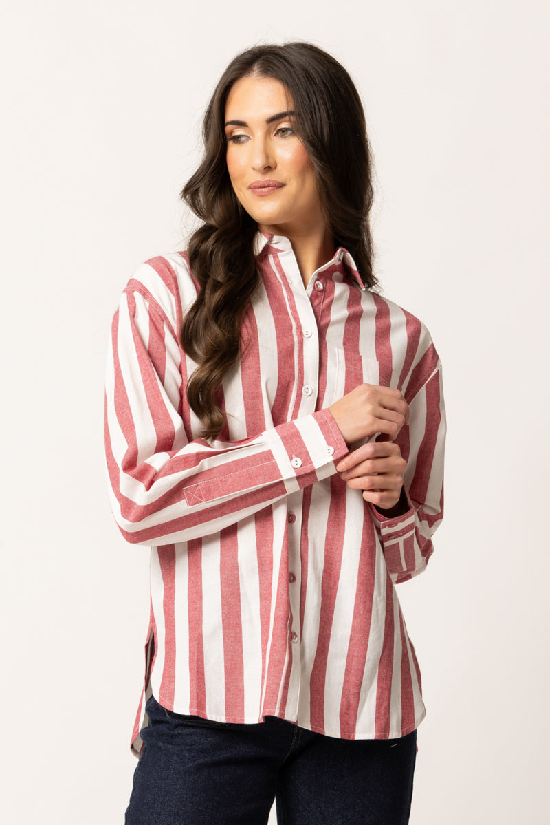 A woman modeling a long-sleeve button-up shirt with vertical red and white stripes, paired with dark blue jeans, against a plain light background.