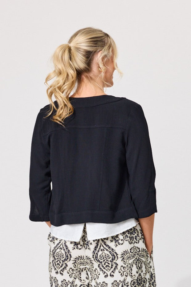 A woman viewed from behind wearing a dark navy cropped three-quarter sleeve top, a white undershirt, and a black and white patterned skirt, against a light gray studio background.
