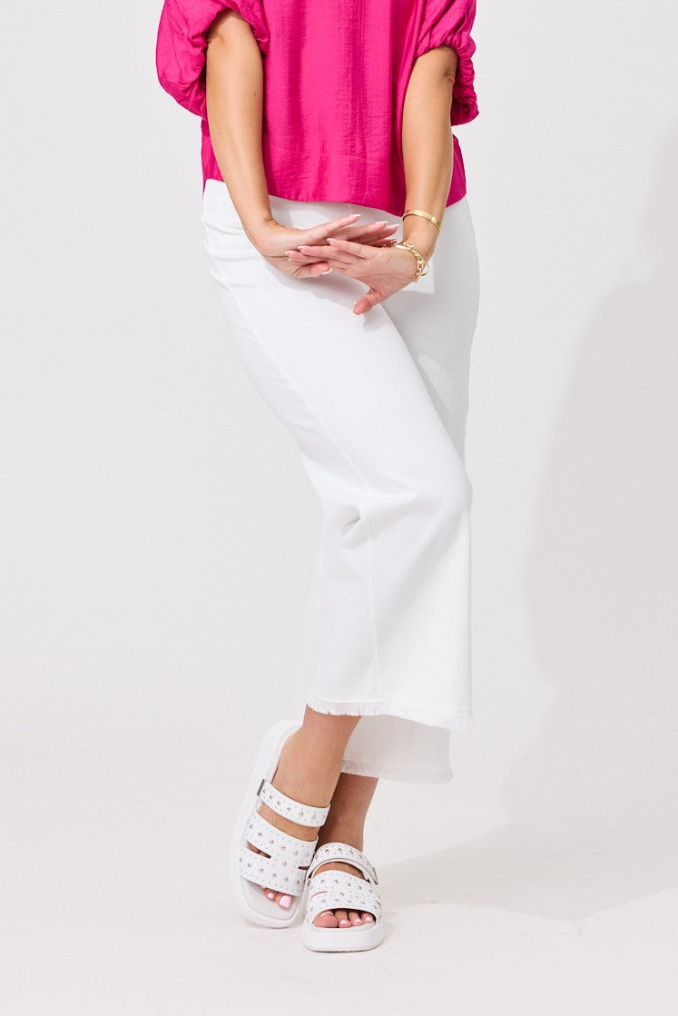 A model wearing white wide-leg cropped pants, a bright pink top, and white platform sandals with silver studs, standing against a plain white studio background.
