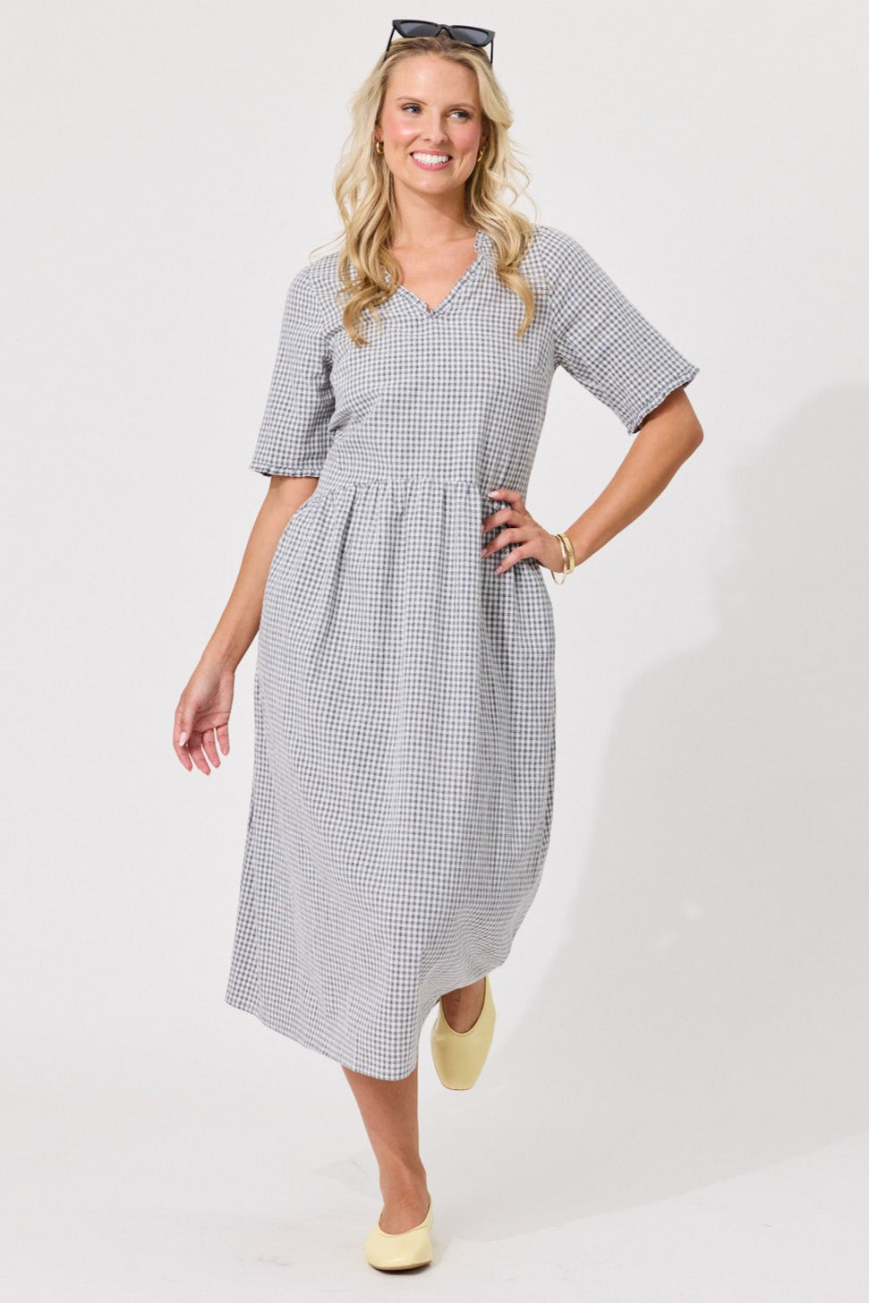 A woman modeling a short-sleeve midi dress with a small black and white gingham pattern, standing against a plain white studio background.