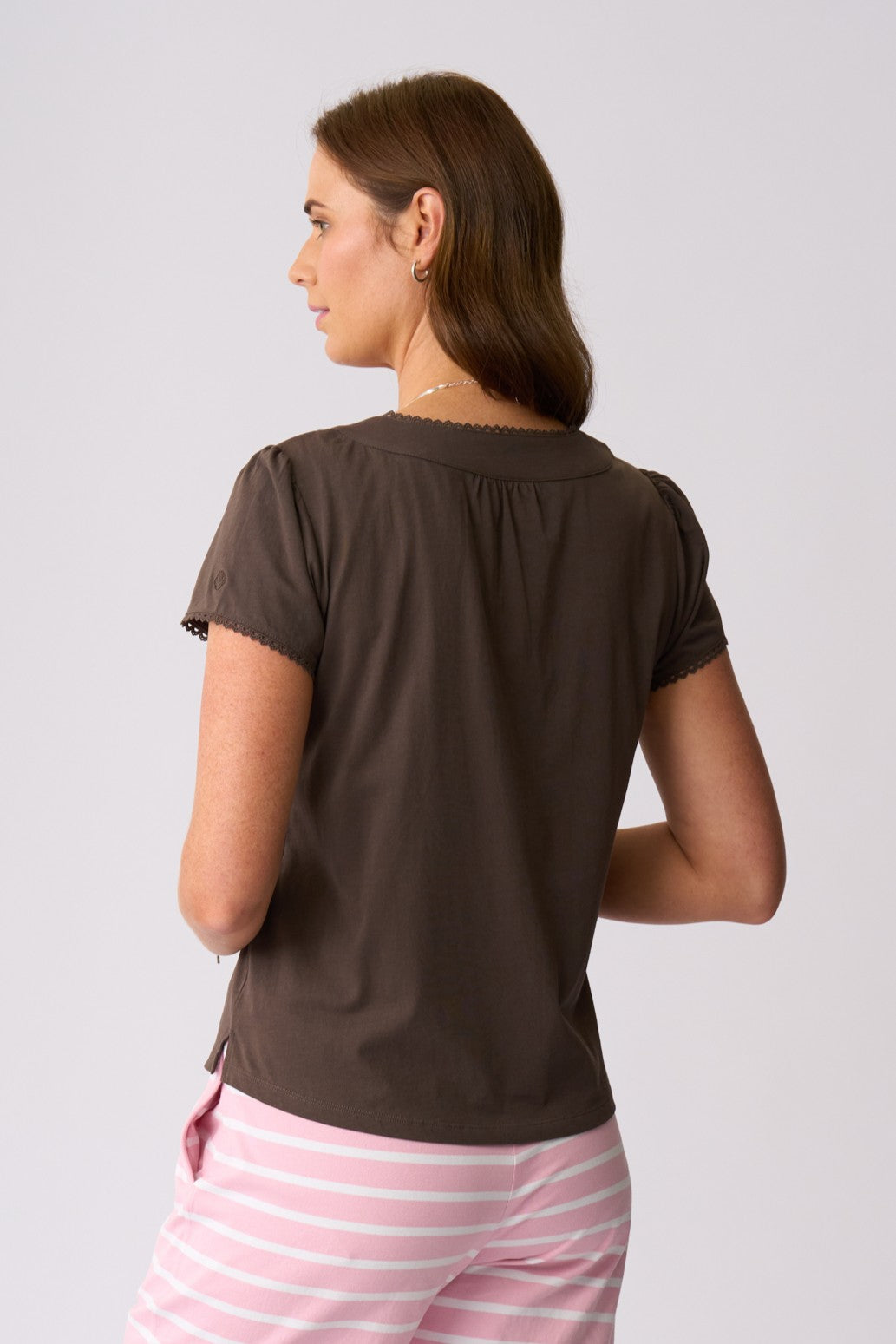 A woman shown from the back wearing a dark brown short-sleeve top and pink and white striped pants against a light gray studio background.