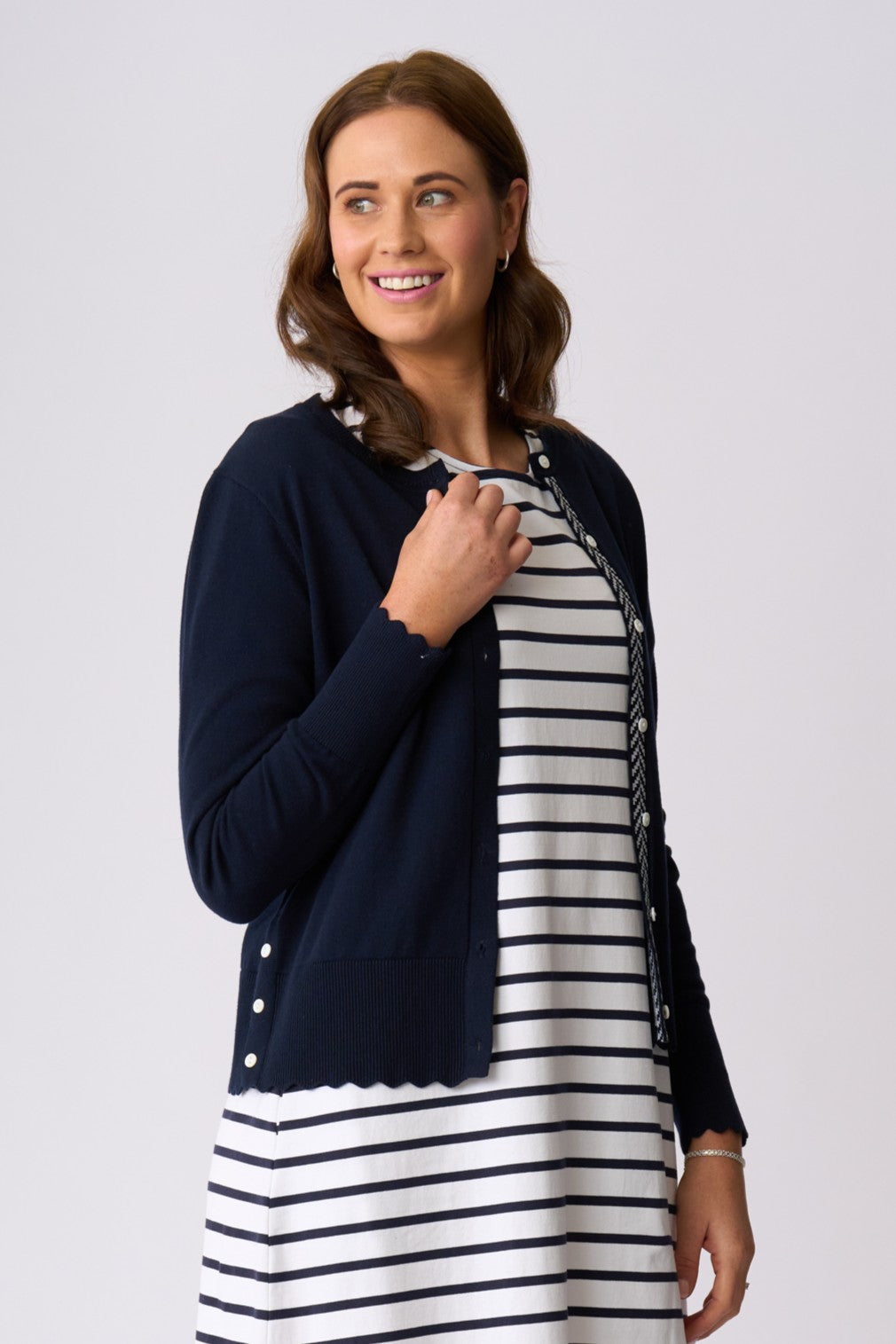 A woman modeling a navy blue cardigan layered over a black and white horizontally striped dress, photographed against a solid light gray studio background.
