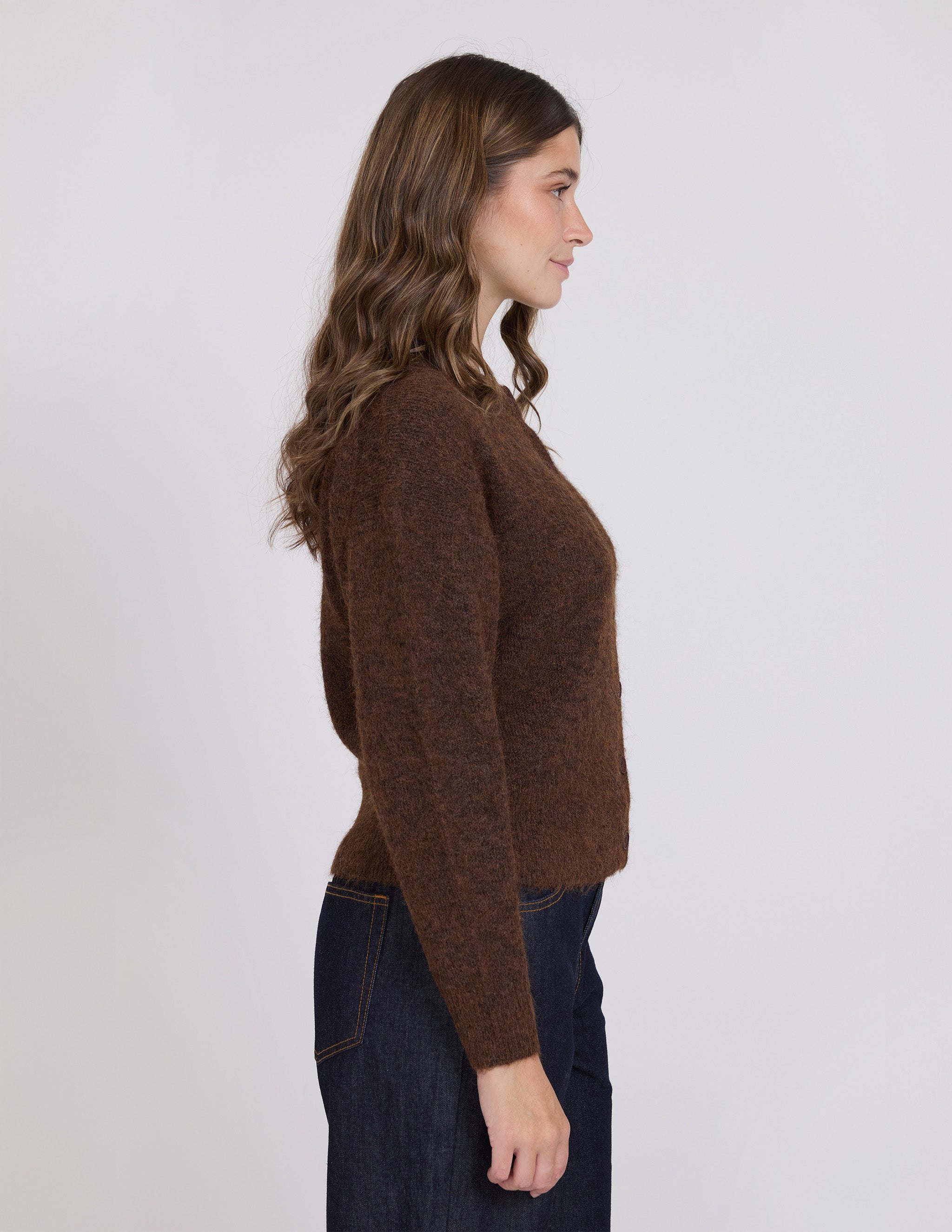 Woman wearing a brown sweater and dark jeans against a white background