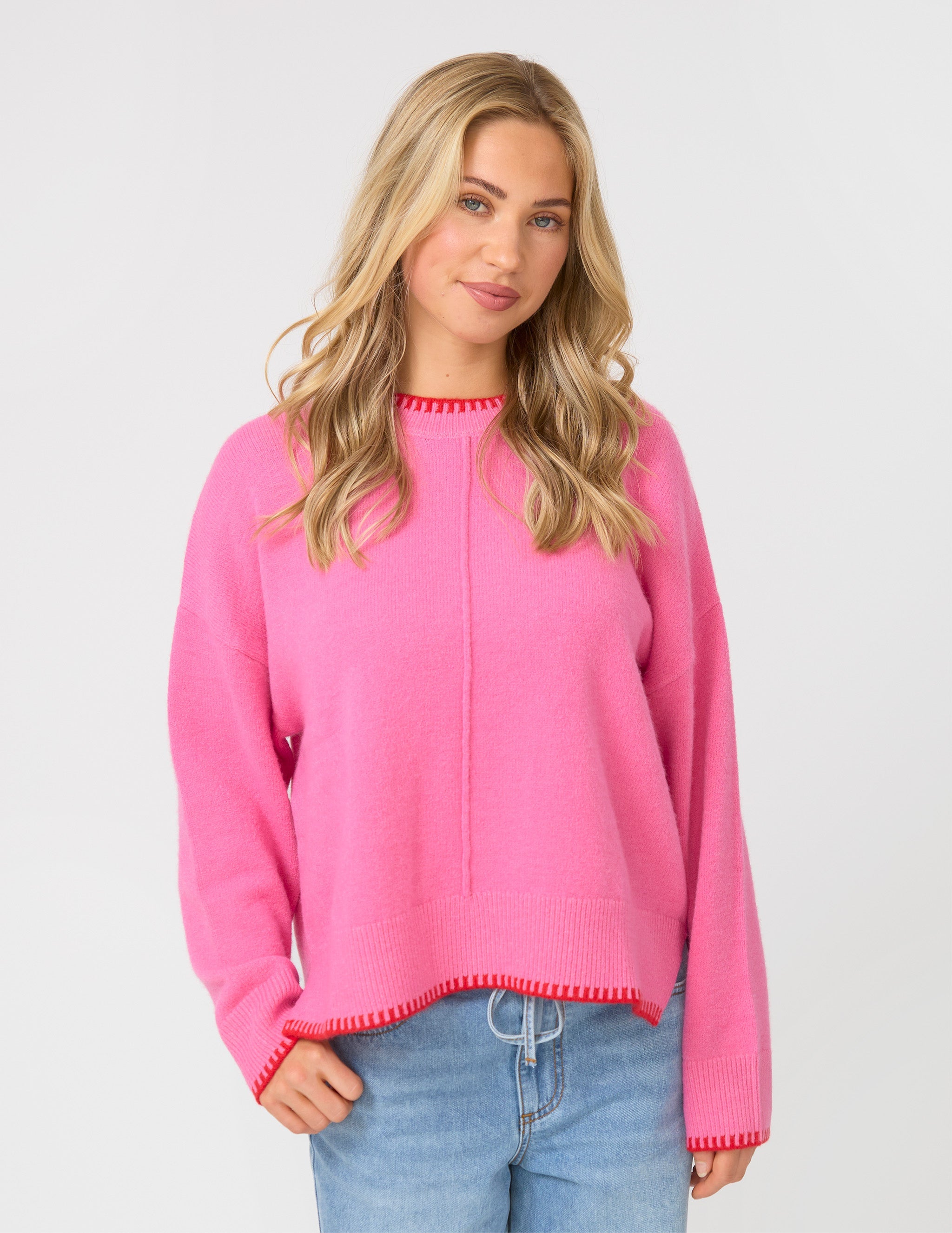 Woman wearing a pink sweater and blue jeans on a white background
