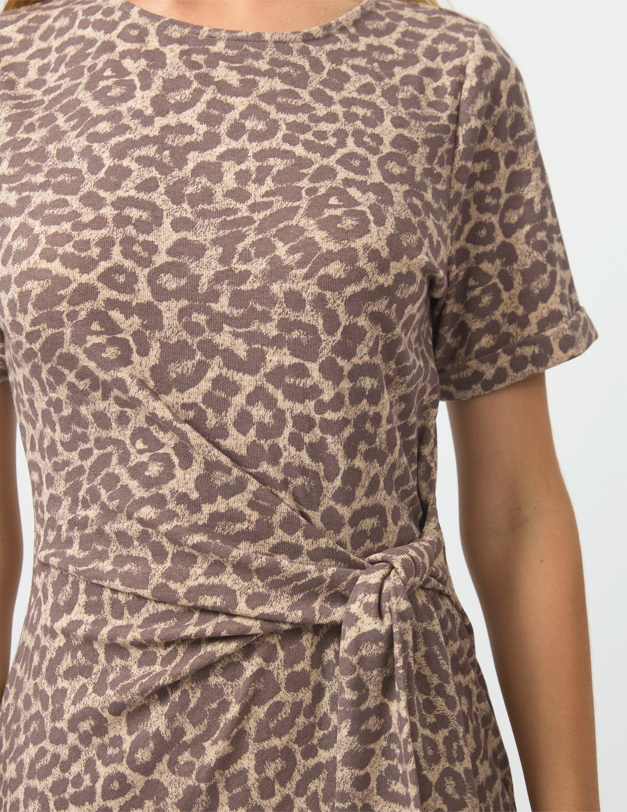 A close-up of a model wearing a short-sleeve wrap dress with a brown and beige leopard print pattern, tied at the waist.