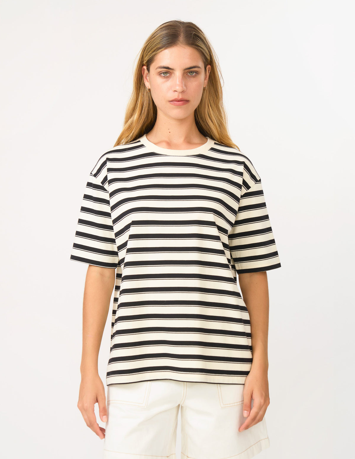 A woman modeling a short-sleeve crewneck t-shirt with horizontal black and off-white stripes, paired with off-white shorts, against a plain white studio background.