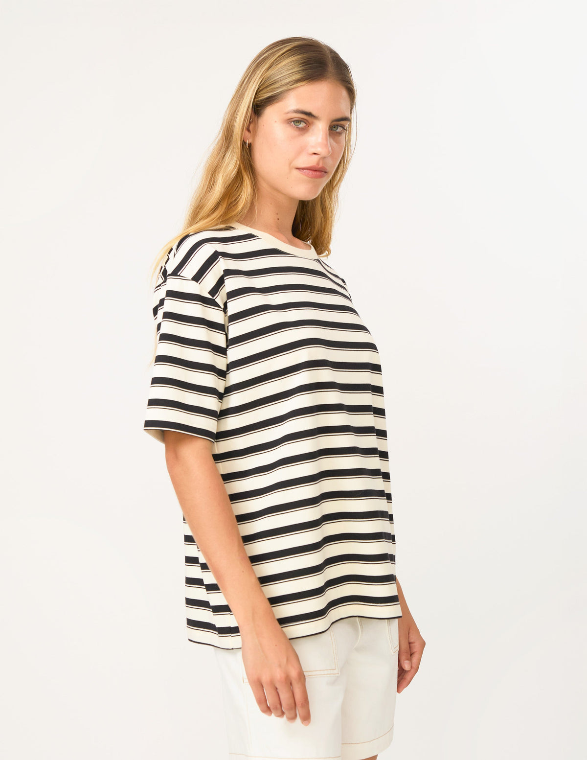 A woman wearing a short-sleeve crewneck top with horizontal black and off-white stripes, paired with off-white shorts, photographed against a plain white studio background.