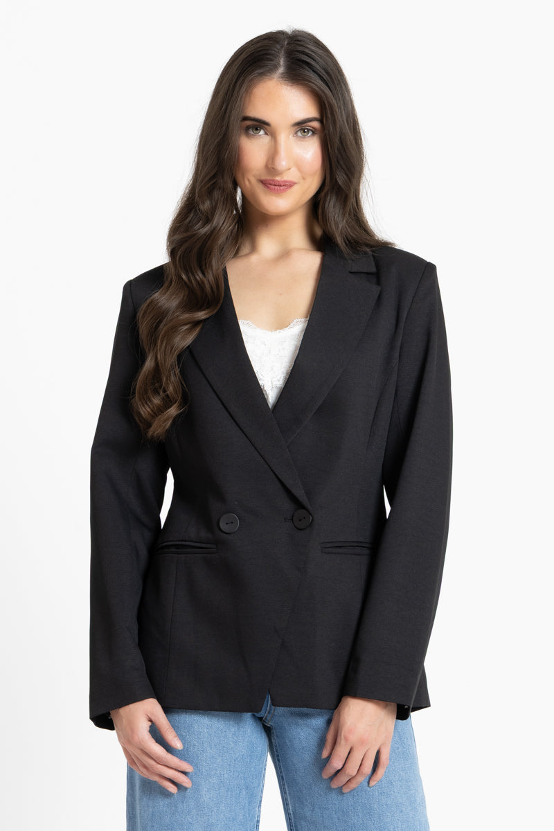 Woman wearing a black blazer over a white top and blue jeans on a white background