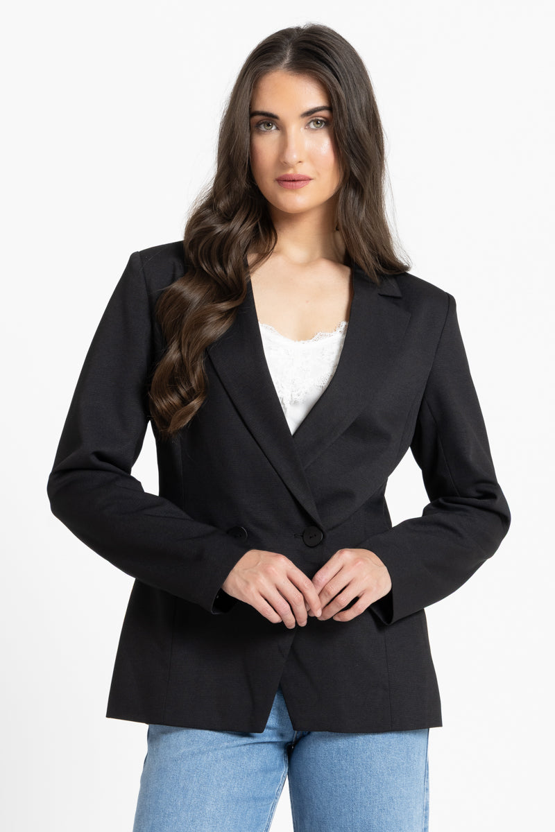Woman wearing a black blazer over a white top and blue jeans on a white background