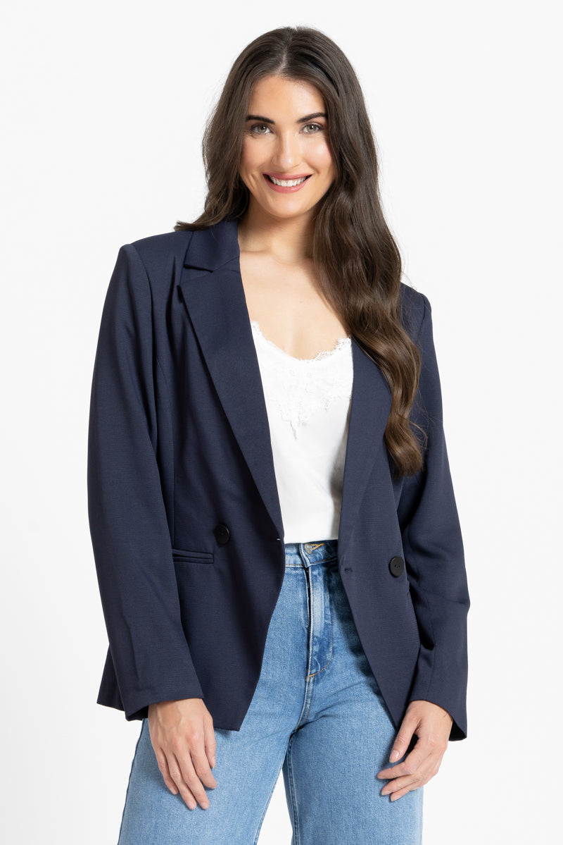Woman wearing a navy blazer over a white top and blue jeans on a white background