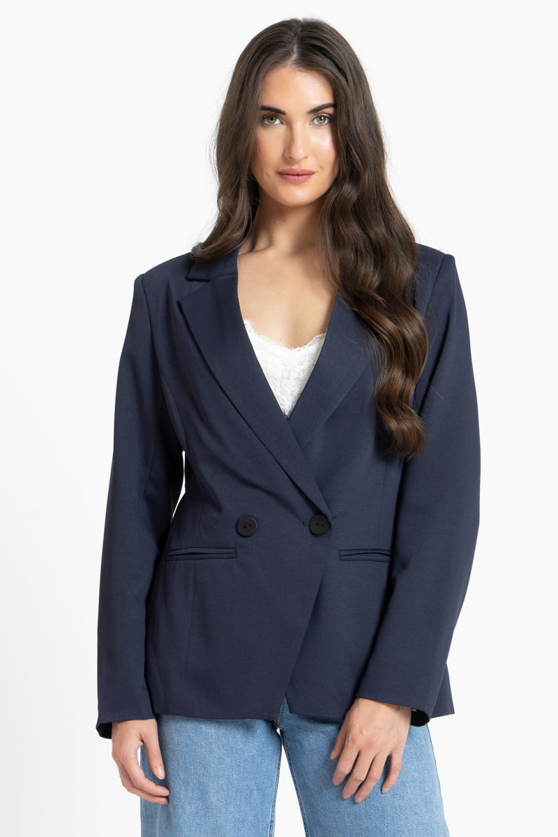 Woman wearing a navy blazer over a white top and blue jeans on a white background