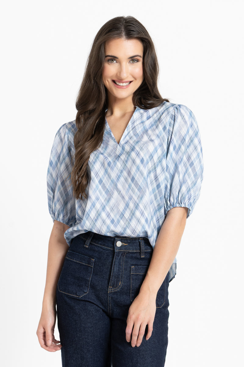 A woman modeling a light blue and white checkered puff-sleeve blouse tucked into dark blue jeans, set against a plain white studio background.