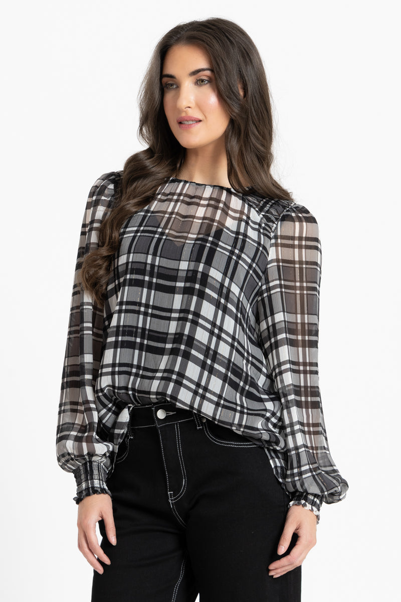 A woman modeling a sheer long-sleeve blouse with a black, white, and gray plaid pattern and balloon sleeves, paired with black pants, against a plain white studio background.