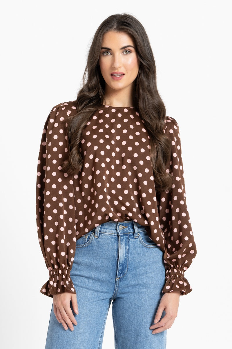 Woman wearing a brown polka dot blouse and blue jeans on a white background