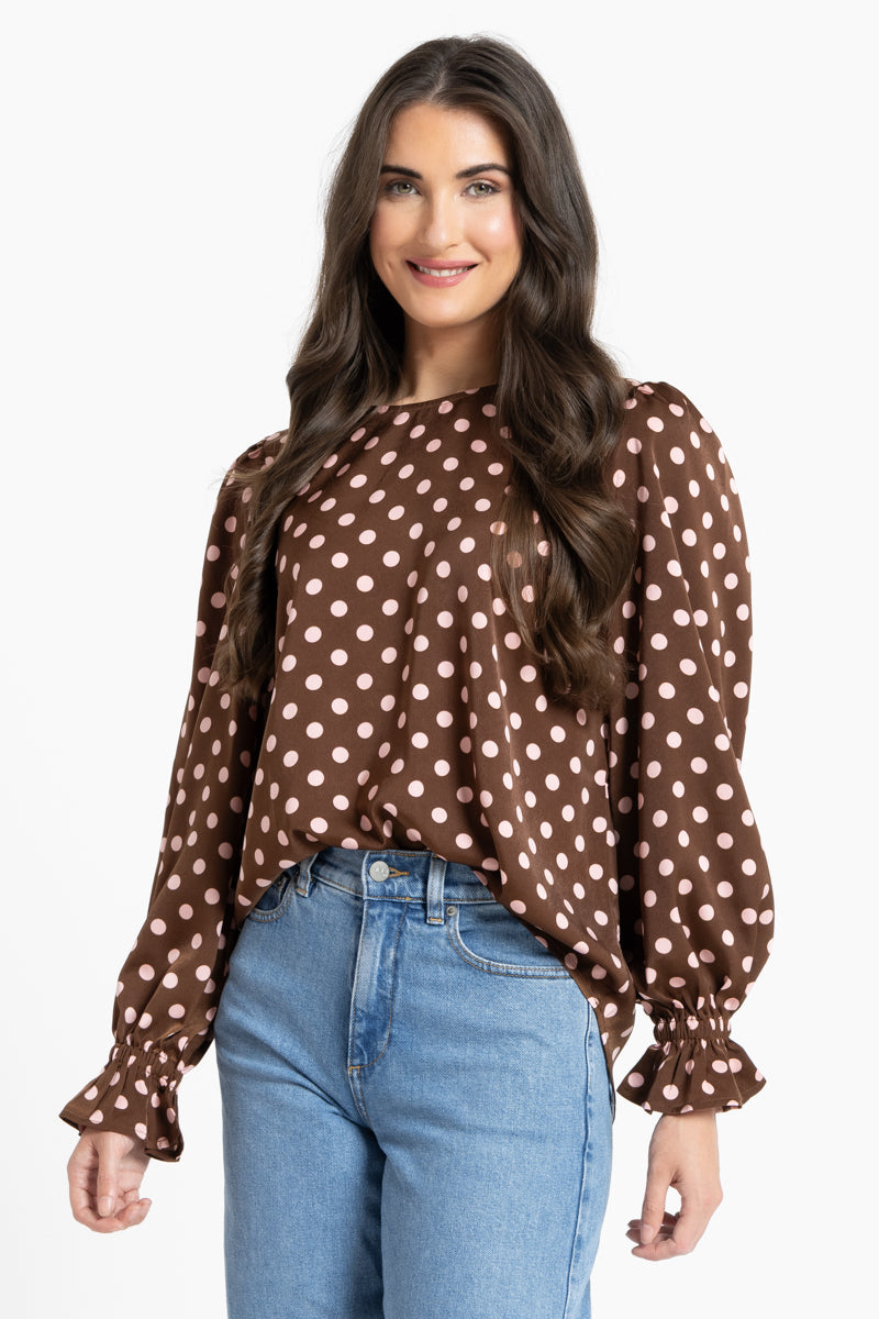 Woman wearing a brown polka dot blouse and blue jeans on a white background
