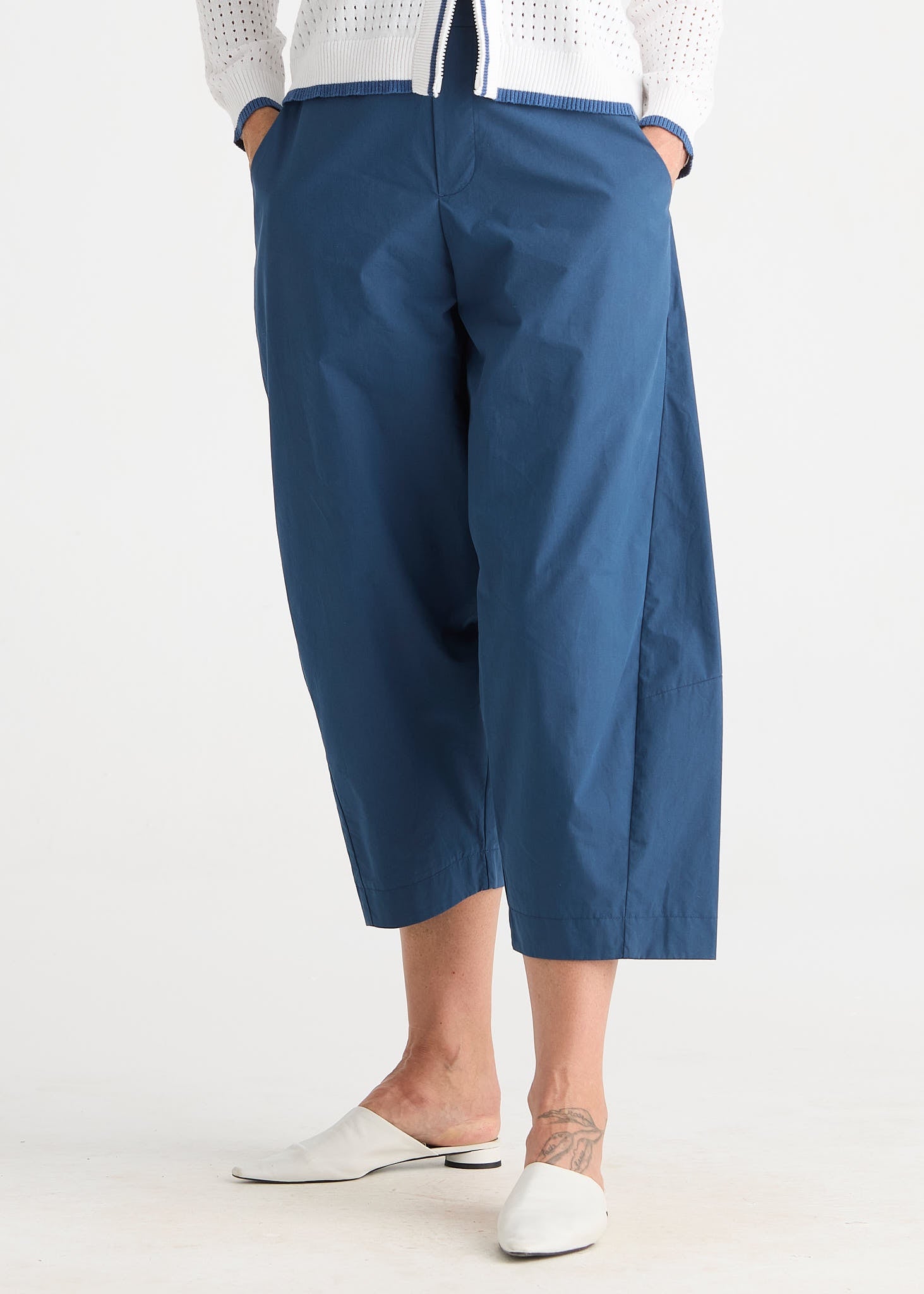 A person wearing blue cropped wide-leg pants with a white knit top and white mule flats, shown from the waist down against a plain light background.