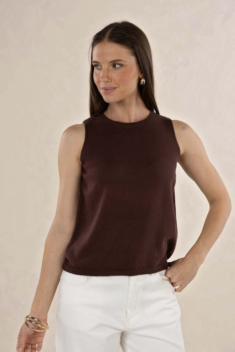 Woman wearing a brown sleeveless top and white pants against a beige background