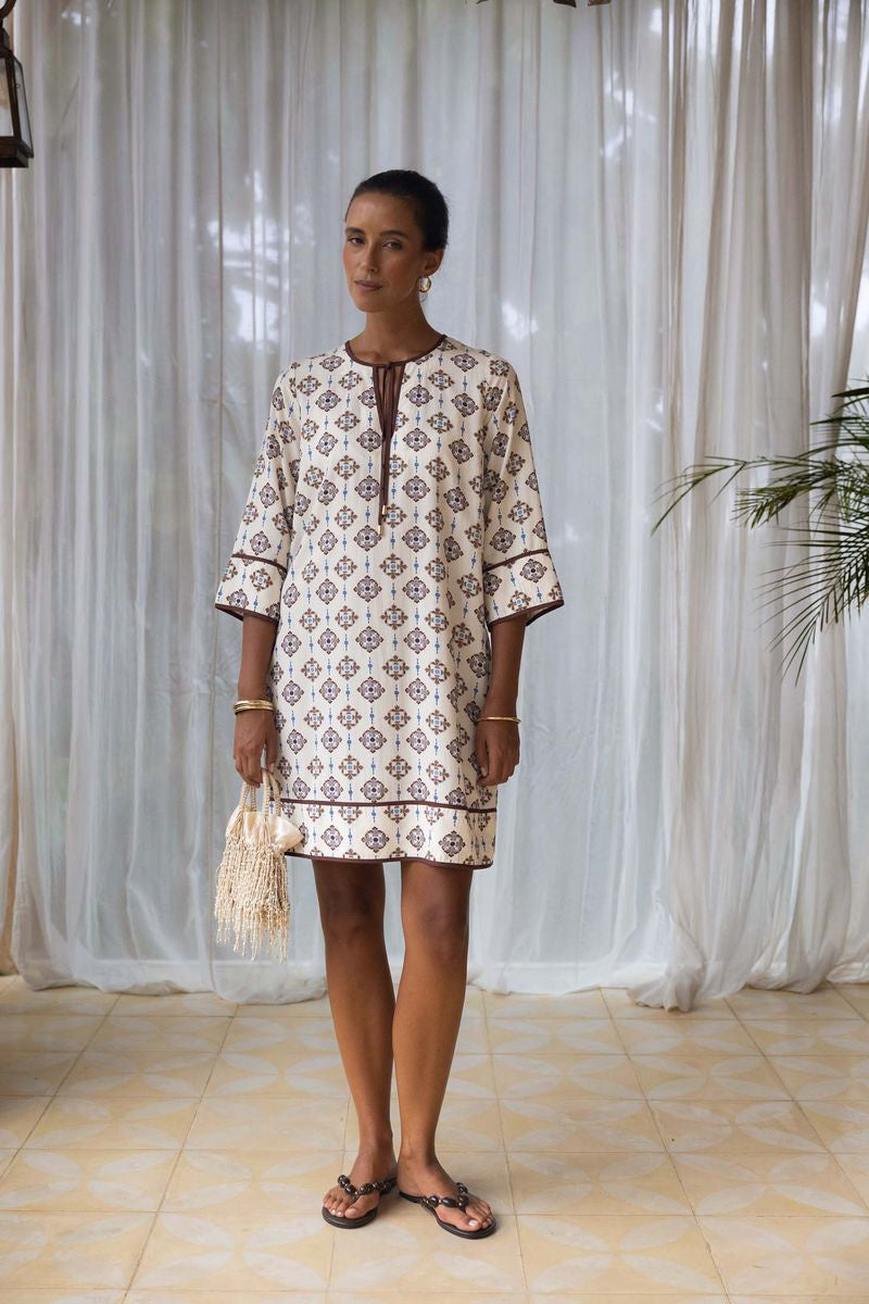 Woman wearing a patterned dress standing in front of white curtains.