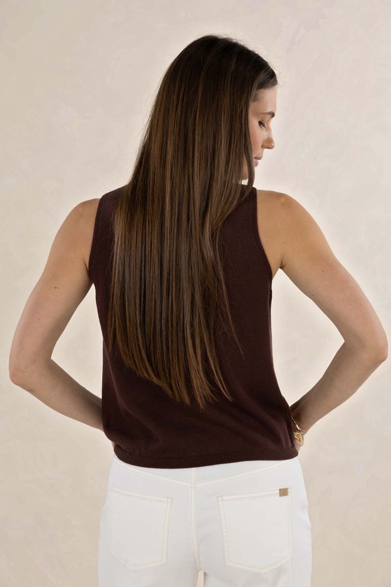 Woman wearing a brown sleeveless top and white pants against a beige background