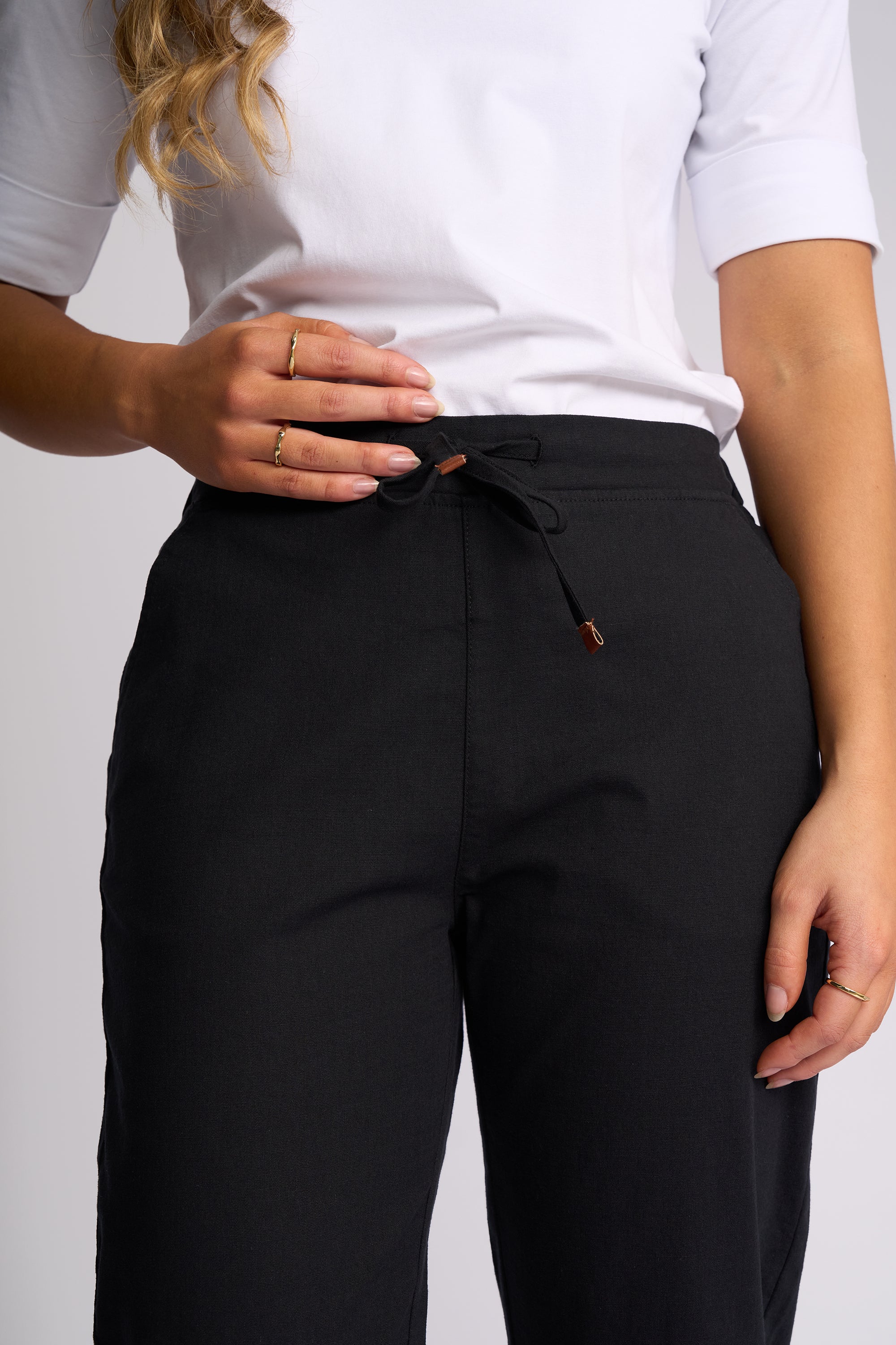 A close-up of a person wearing black drawstring trousers and a white short-sleeve top against a light gray studio background.