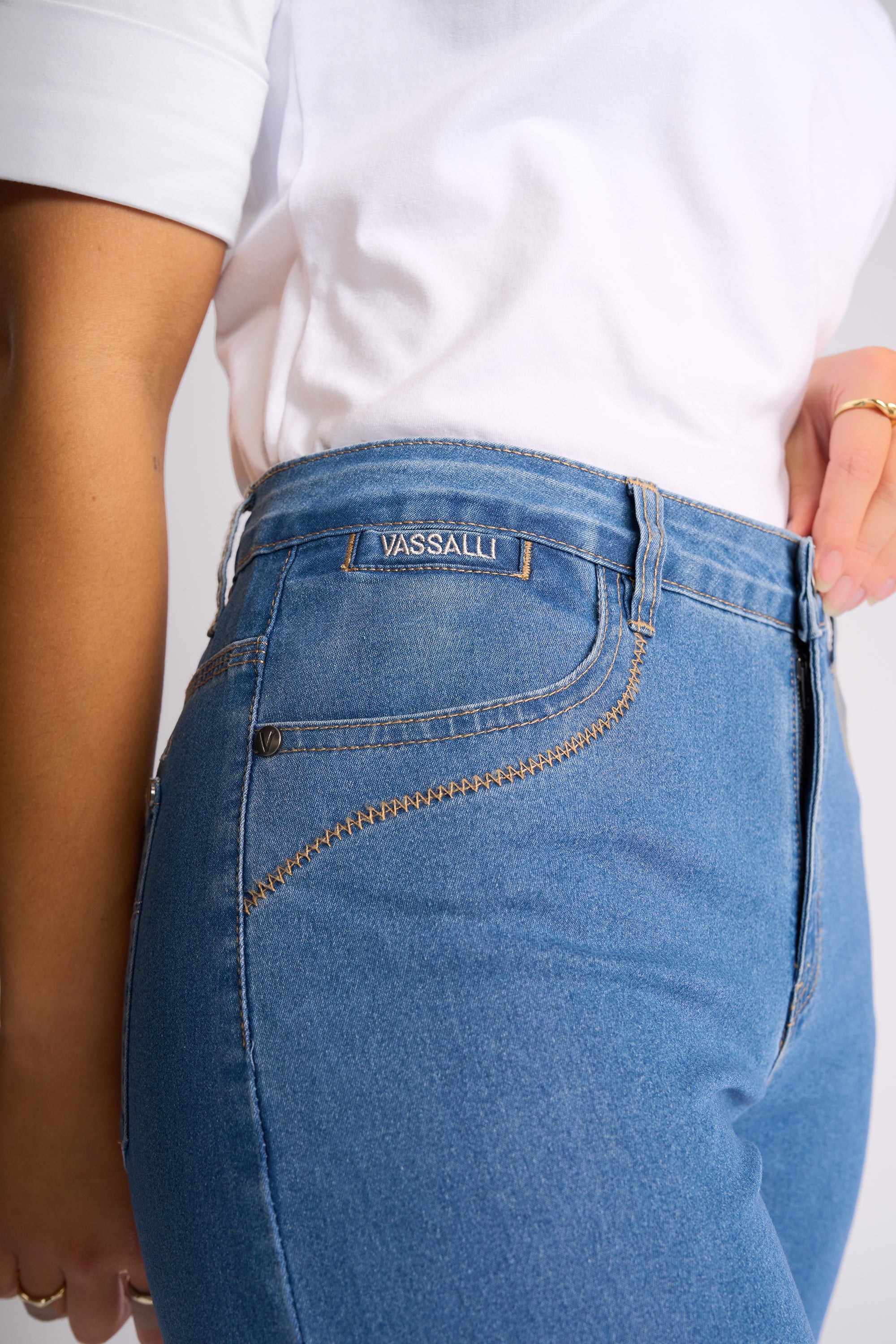 Close-up of a person wearing blue denim jeans with a white t-shirt, showing the back pocket and waistband of the jeans. The brand name 'WASSALL' is clearly visible on the back pocket label.