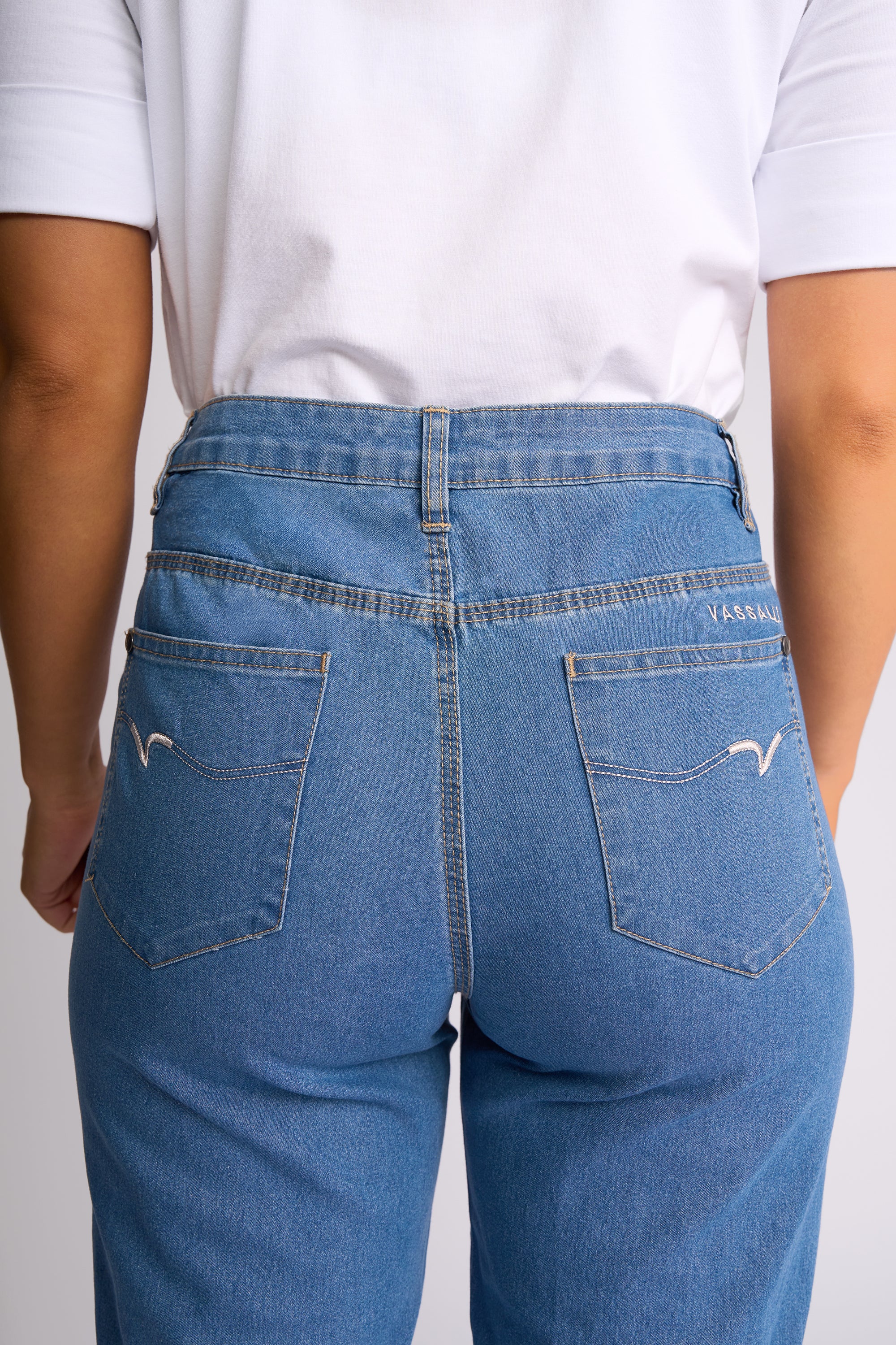 Rear view of a person wearing light blue denim jeans with a white t-shirt, showing the back pockets and stitching details.