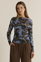 Woman wearing a long-sleeve floral top and brown pants on a beige background