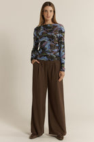 Woman wearing a patterned top and brown pants on a beige background