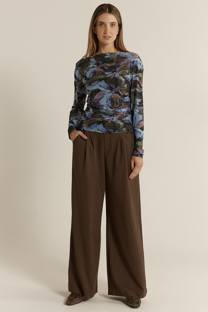 Woman wearing a patterned top and brown pants on a beige background