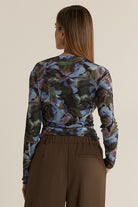 Woman wearing a long-sleeve floral top and brown pants on a beige background