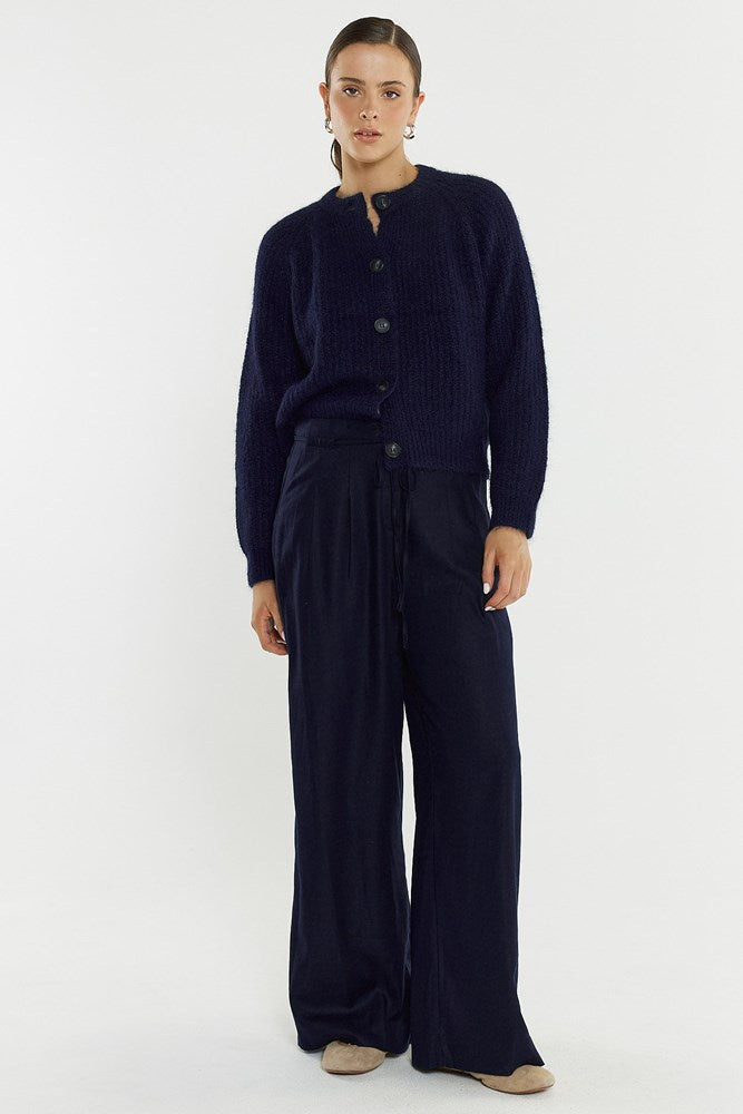 Person wearing a navy blue cardigan and pants on a white background