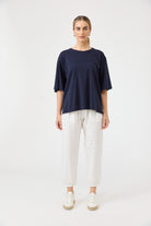 Woman wearing a navy blue top and white pants on a white background