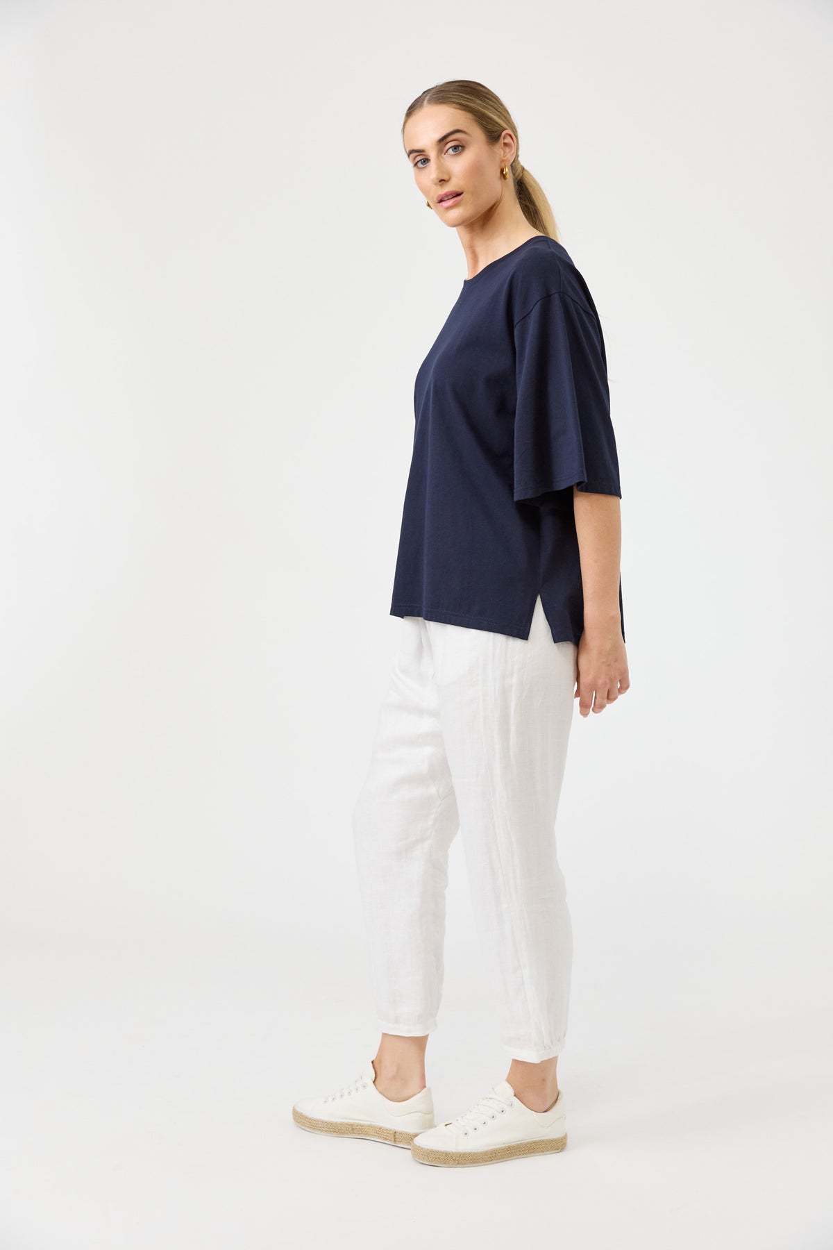 Woman wearing a navy blue top and white pants on a white background
