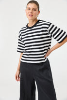 Woman wearing a black and white striped sweater with wide-leg pants on a plain background