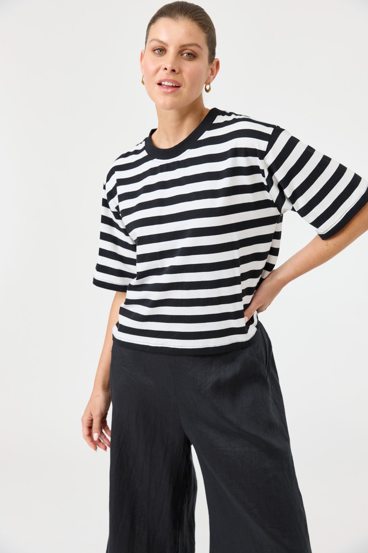 Woman wearing a black and white striped sweater with wide-leg pants on a plain background