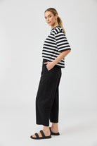 Woman wearing a black and white striped shirt and black pants on a white background