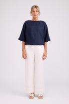 A woman modeling a navy blue short-sleeve top and white wide-leg trousers against a light gray studio background.