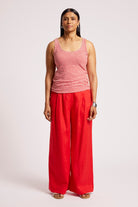 A woman modeling a sleeveless red and white striped tank top paired with bright red wide-leg pants, standing against a light gray studio background.