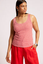 A woman wearing a red and white horizontally striped tank top and bright red wide-leg pants, photographed against a light gray studio background.