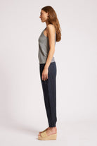 A woman shown in profile wearing a sleeveless black and white striped top, dark navy pants, and beige platform sandals against a plain light gray studio background.
