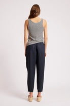 A woman shown from the back wearing a sleeveless black and white striped top and dark navy pants, standing against a plain light gray studio background.