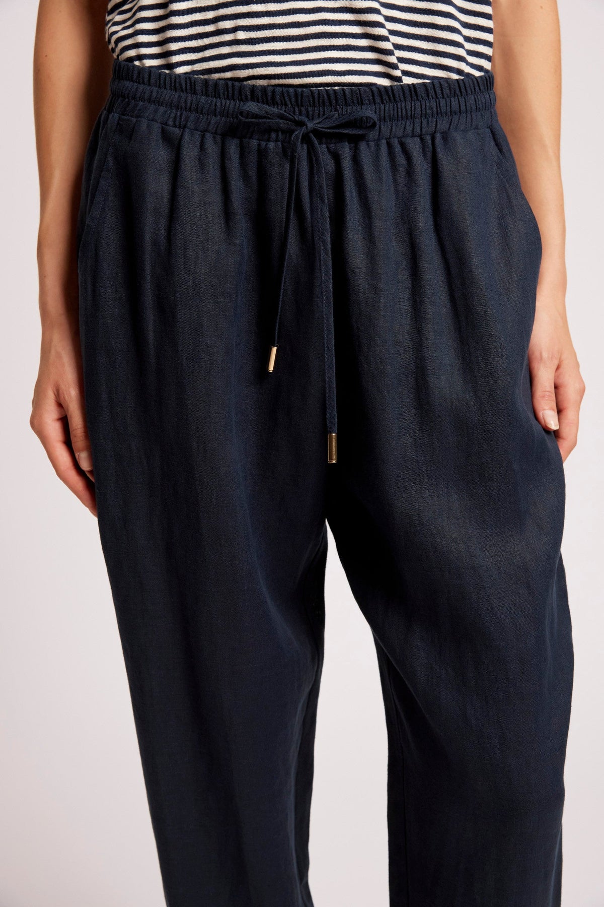 A close-up of a person wearing dark navy drawstring trousers with a striped top partially visible at the top edge, against a plain light background.