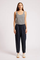 A woman modeling a sleeveless black and white striped tank top paired with dark navy drawstring pants and beige sneakers, standing against a light gray studio background.