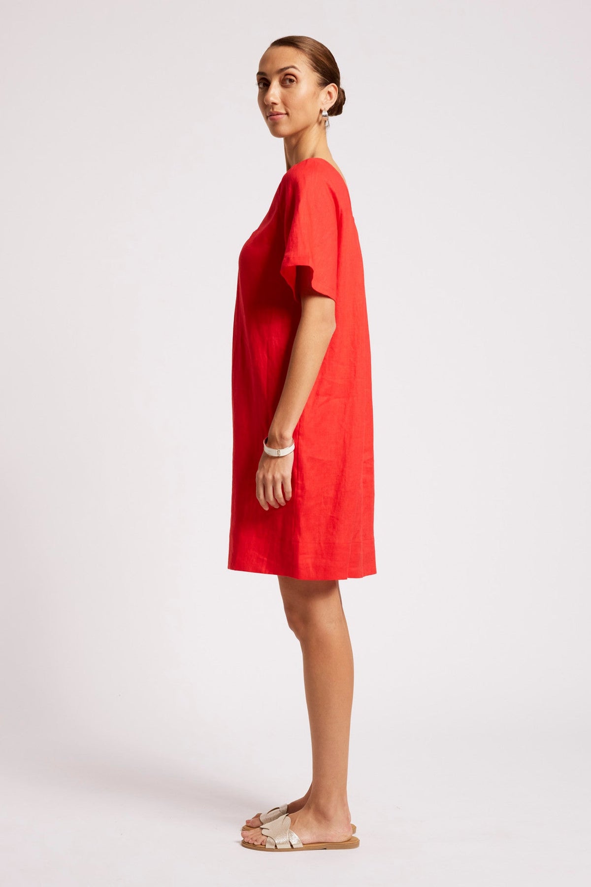 A woman modeling a bright red short-sleeve linen dress, shown in profile against a plain light gray studio background.